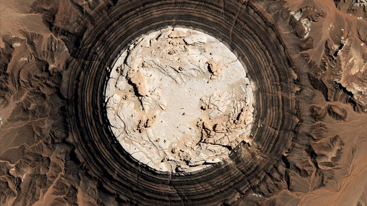 Top-down illustration of a bright pale rock massif surrounded by darker banded terrain
