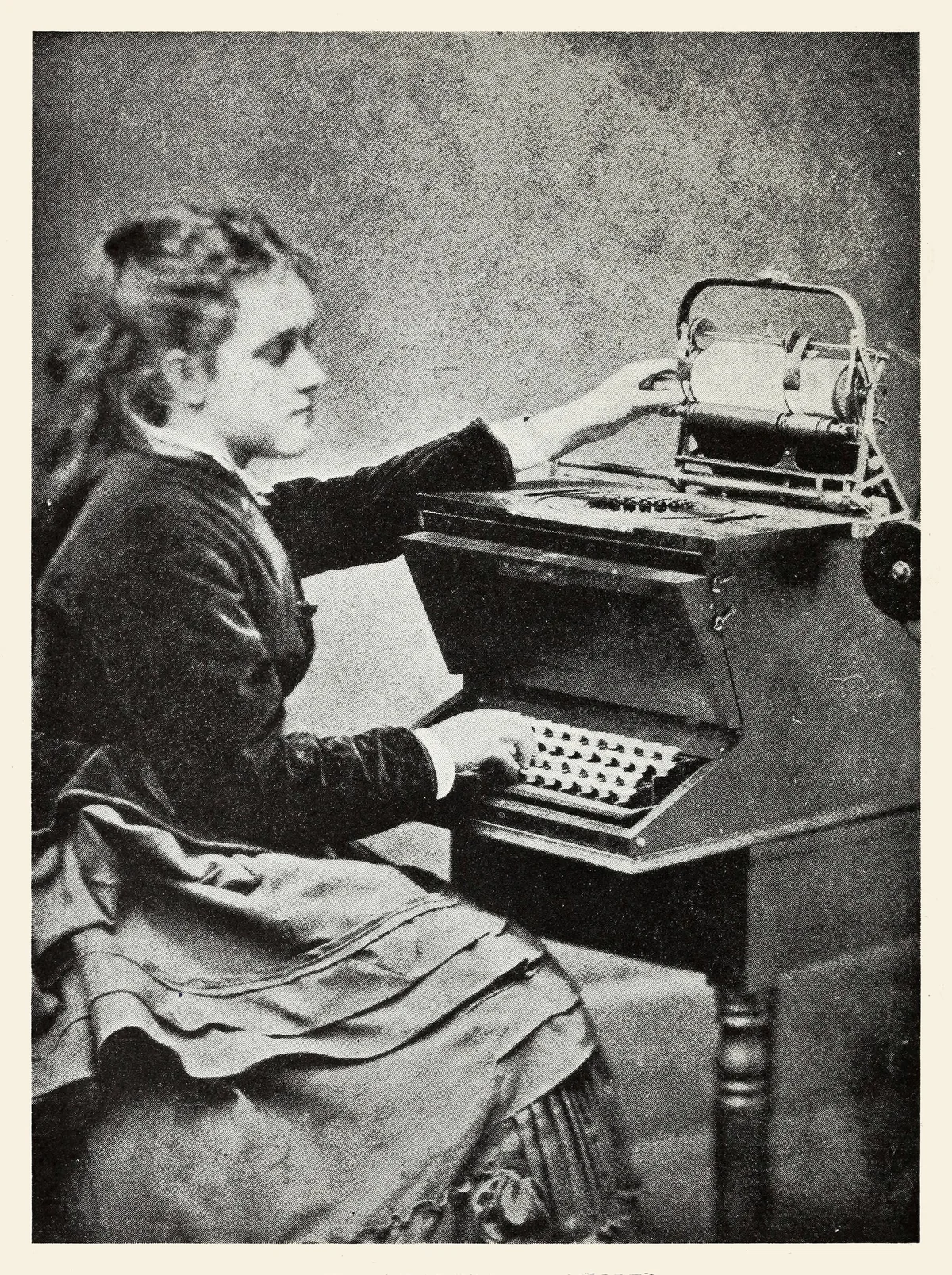 Lillian Sholes seated at an early typewriter prototype in 1872, in a long dress with her hands over the keys