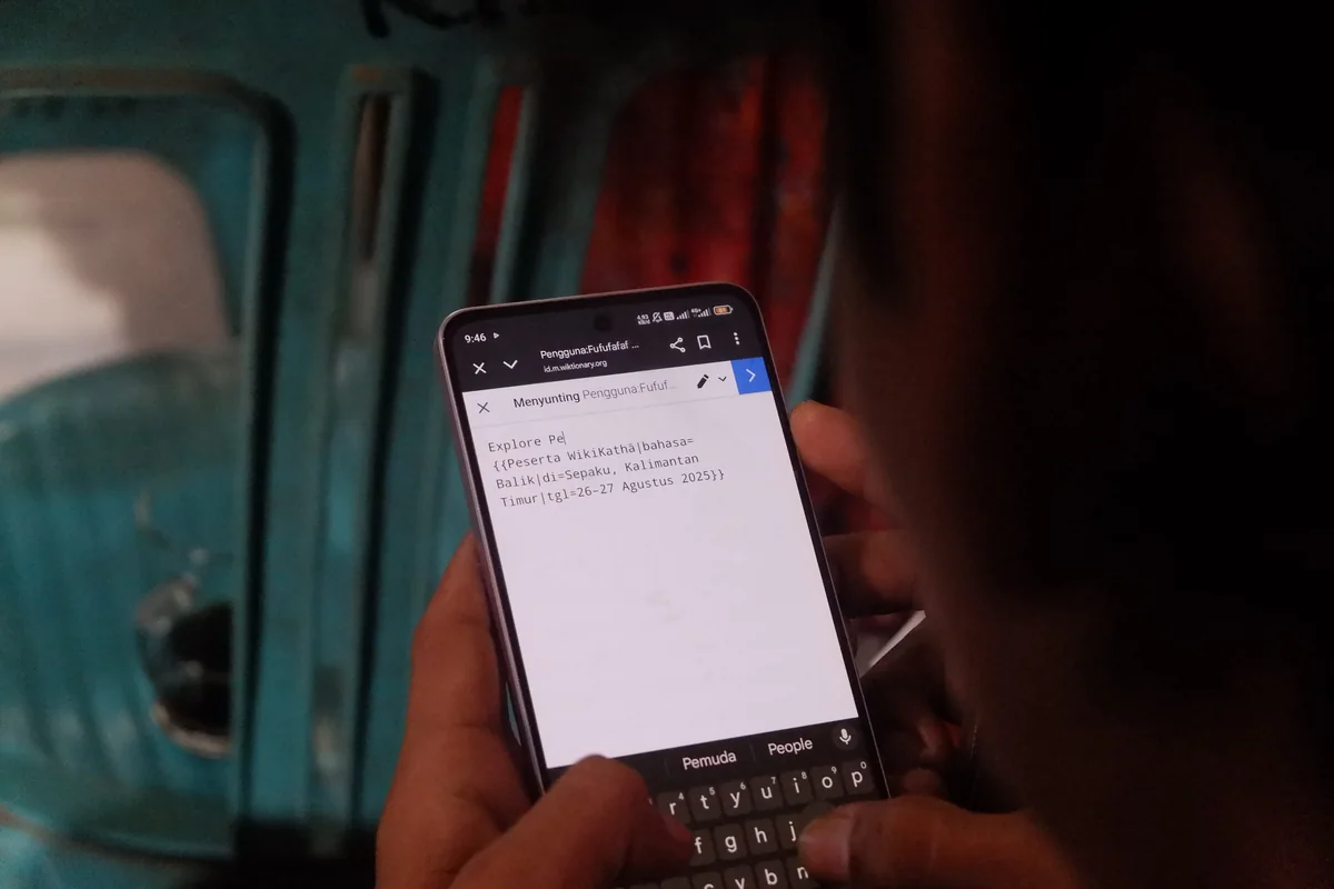 Close-up of hands typing on a smartphone during the WikiKathā editing workshop in Sepaku, East Kalimantan